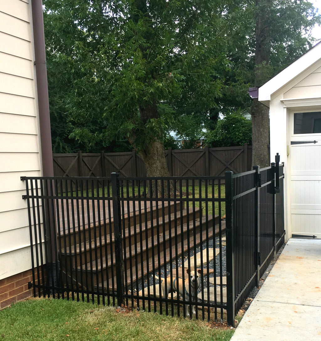 Black metal aluminum fence for pet security with a house and trees in the background.