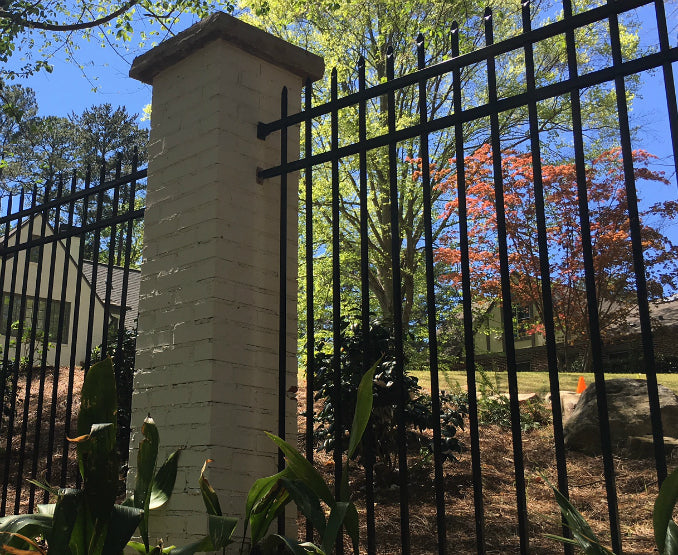 Black metal fence with aluminum wall brackets with a stone pillar in a garden setting