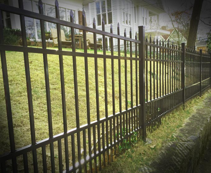 Metal fence with decorative top rail puppy pickets in front of a house and garden.