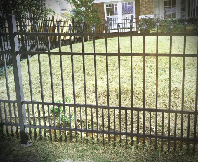 Metal fence with spear top and puppy pickets with a view of a grassy yard and house in the background