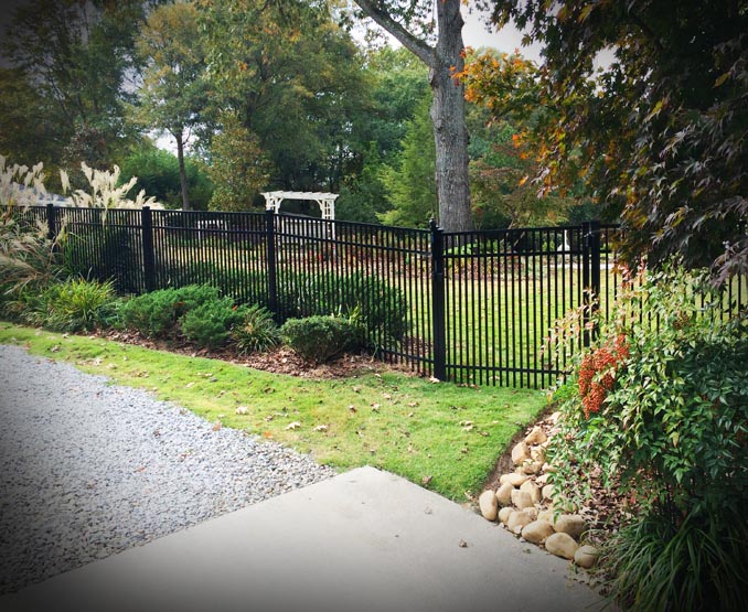 Black metal fence along a driveway with trees and greenery in the background