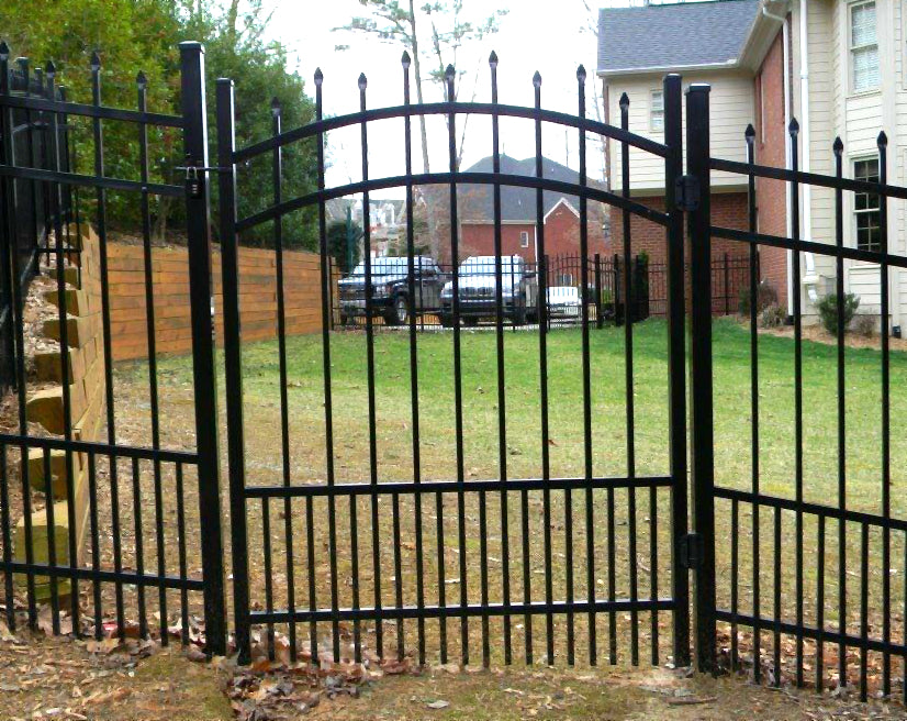 Black metal fence with a gate in front of a house and parked cars.