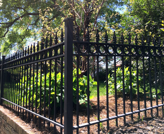 Black metal fence with decorative aluminum rings and finials in a garden setting