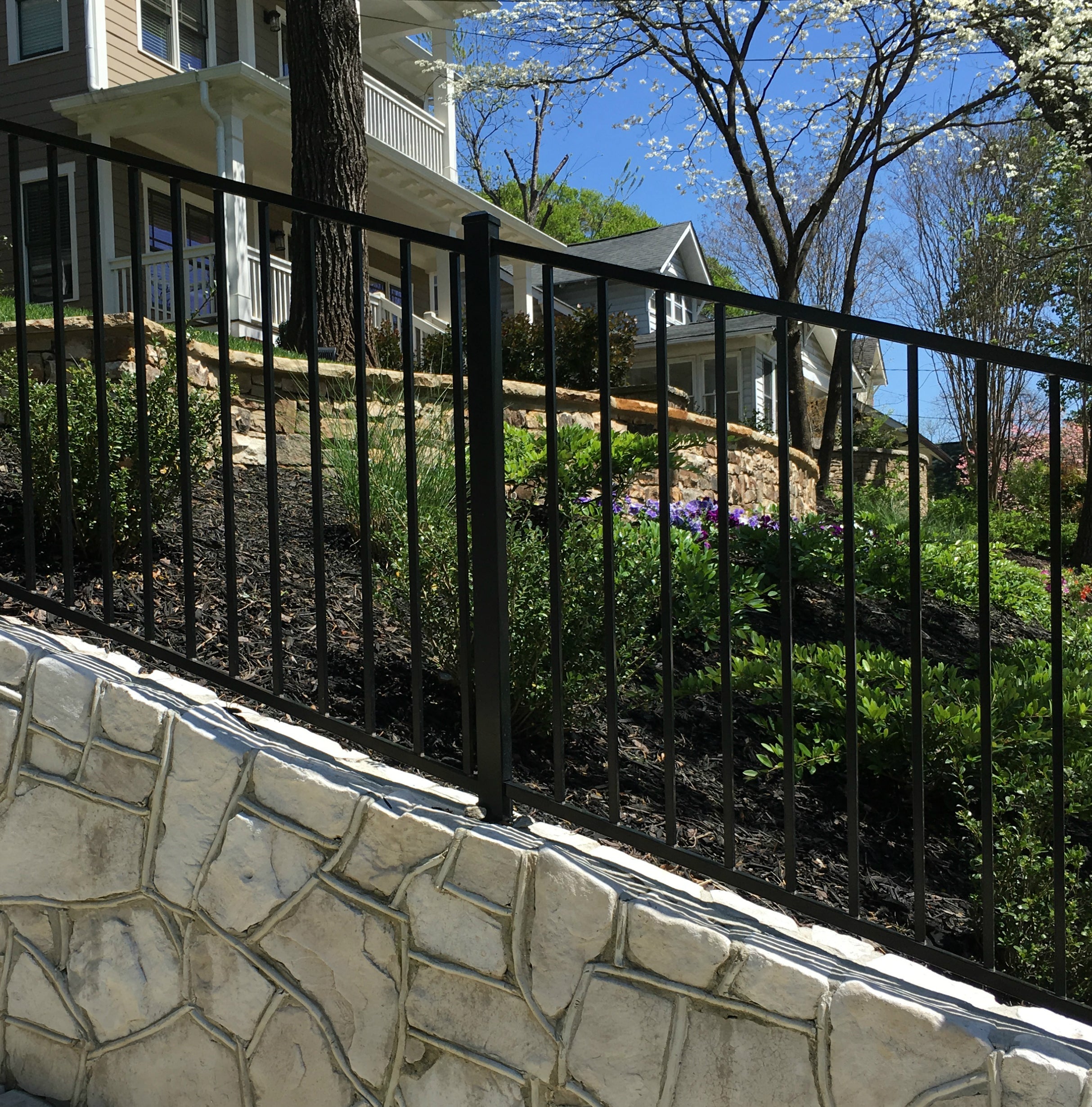 Black metal fence with stone foundation in front of a house on a slope.