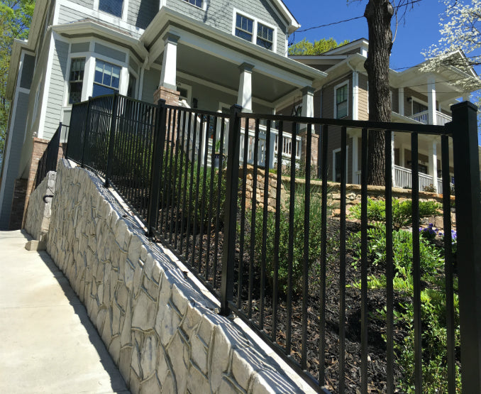 Black metal fence 2-rail aluminum fence on a slope with stone wall and house in background