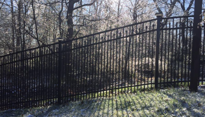 Black metal aluminum fence with trees and snow on the ground