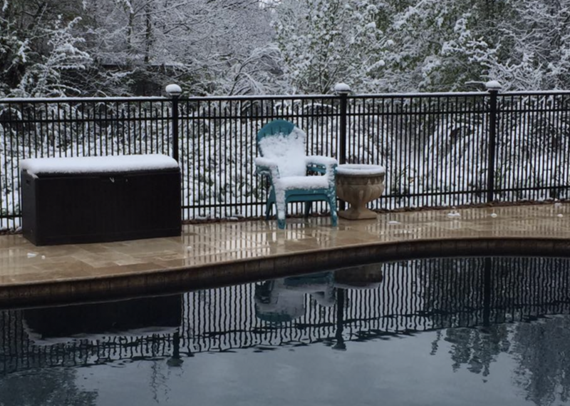 Pool area with snow-covered furniture and aluminum fence during a snowfall
