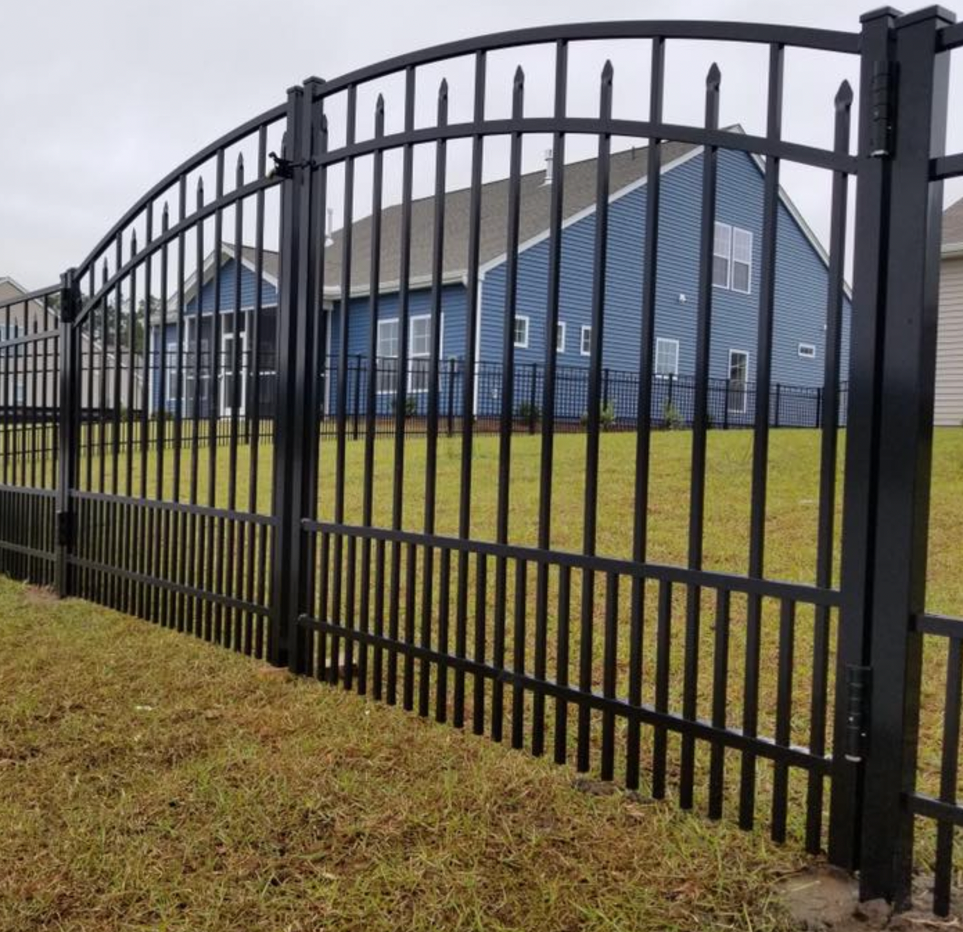 Black metal fence with pet security in front of a blue house with gray roof