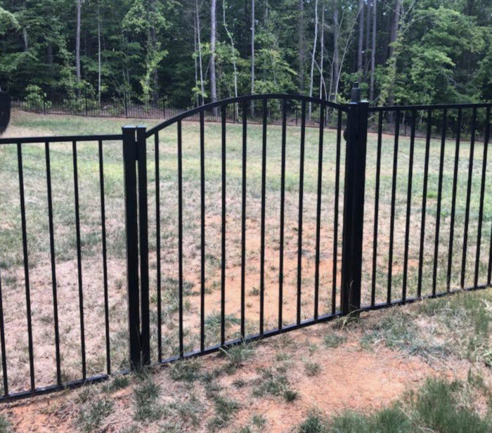 Black metal fence in a grassy area with trees in the background