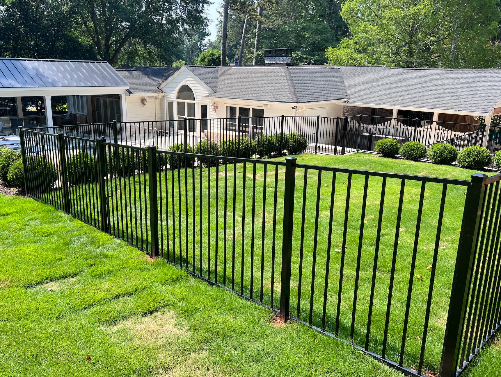 Black metal fence 2-rail aluminum fence front of a building with green grass and trees in the background
