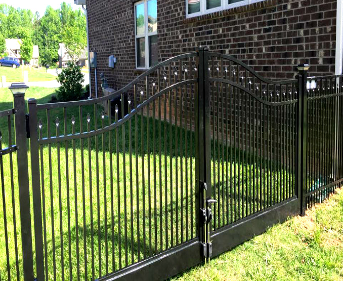 Black metal aluminum fence with decorative top rail, estate arch and solid bottom rail for automation in front of a brick house