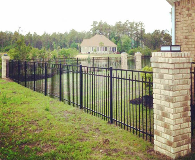 Black metal fence with brick pillars near a body of water and house.