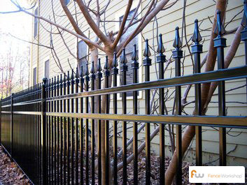 Black metal aluminum fence with decorative aluminum finials against a building and tree